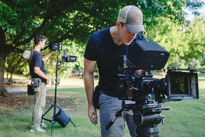 Two male film crew members setting up filming equipment outside